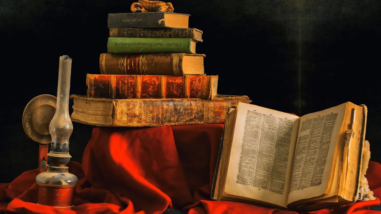 An artistic still life featuring a stack of vintage books and an olive lamp on rich red cloth.